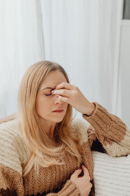 Woman sitting with a headache, wearing a cozy sweater in an indoor setting.